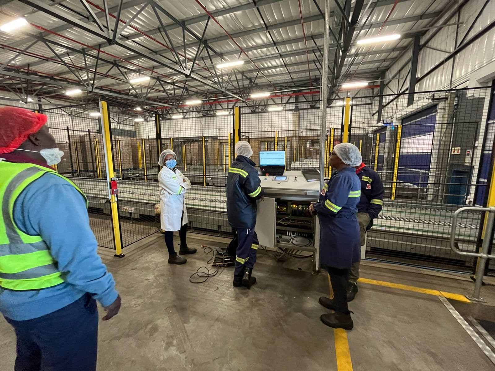 Engineers and plant staff in hairnets around an HMI during commissioning of a food production line.
