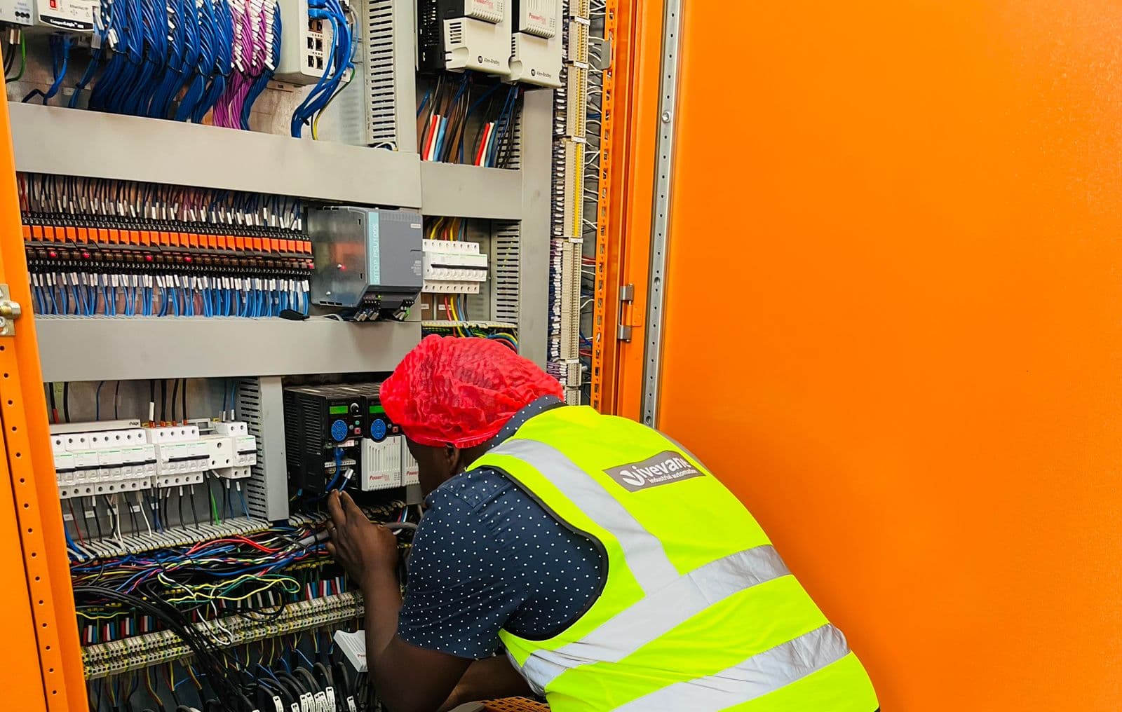 An Ivevane engineer in branded PPE and a hairnet wiring drives inside an orange control panel in a food plant.
