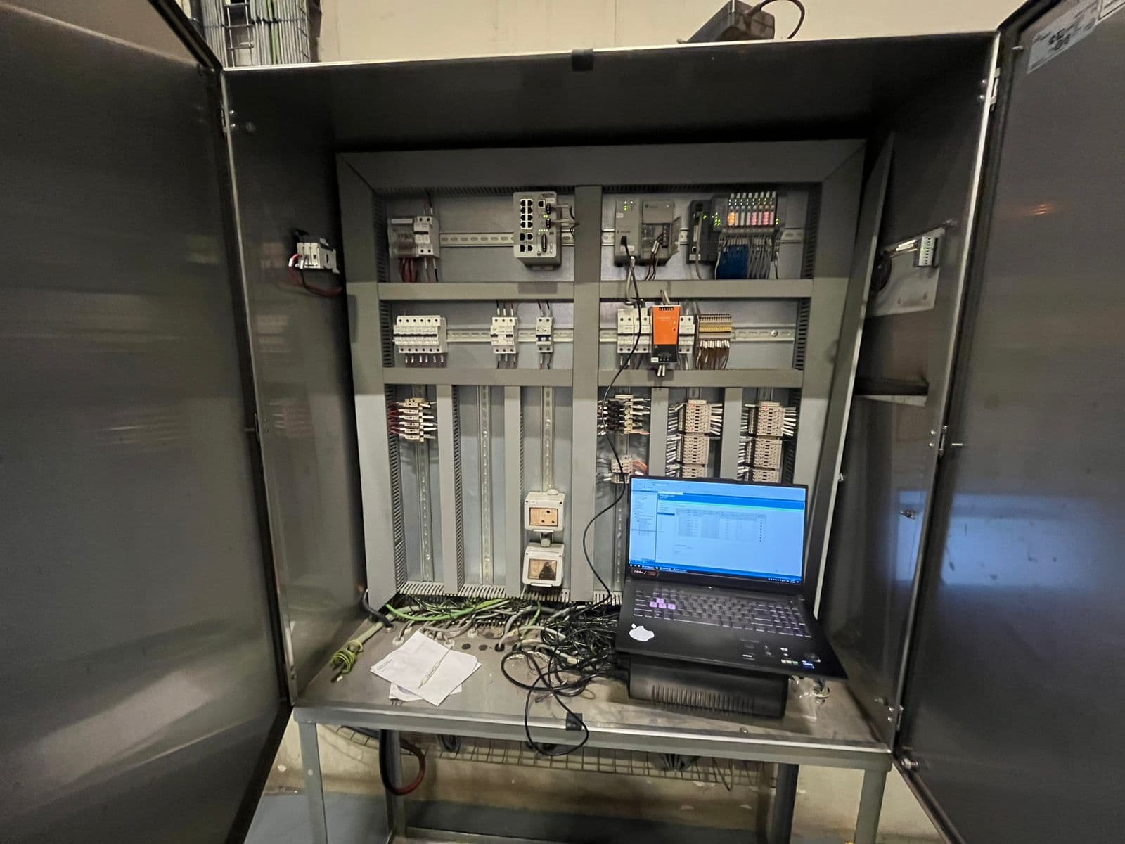 Control cabinet opened for commissioning, with a managed network switch, distributed I/O and a laptop connected to the controller.
