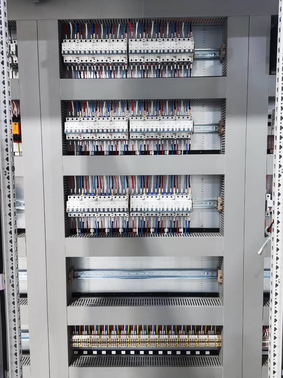 Interior of an Ivevane-built motor control centre: rows of miniature circuit breakers on DIN rail with colour-coded wiring runs and numbered terminal blocks.