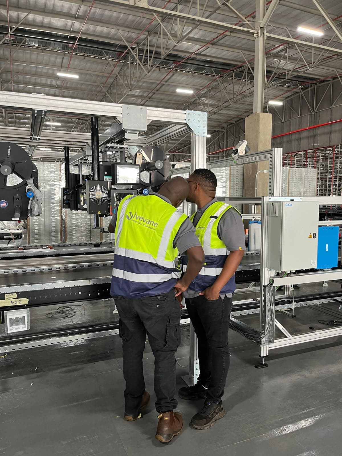 Ivevane engineers on a customer site checking an automated line against a SICK safety controller cabinet.