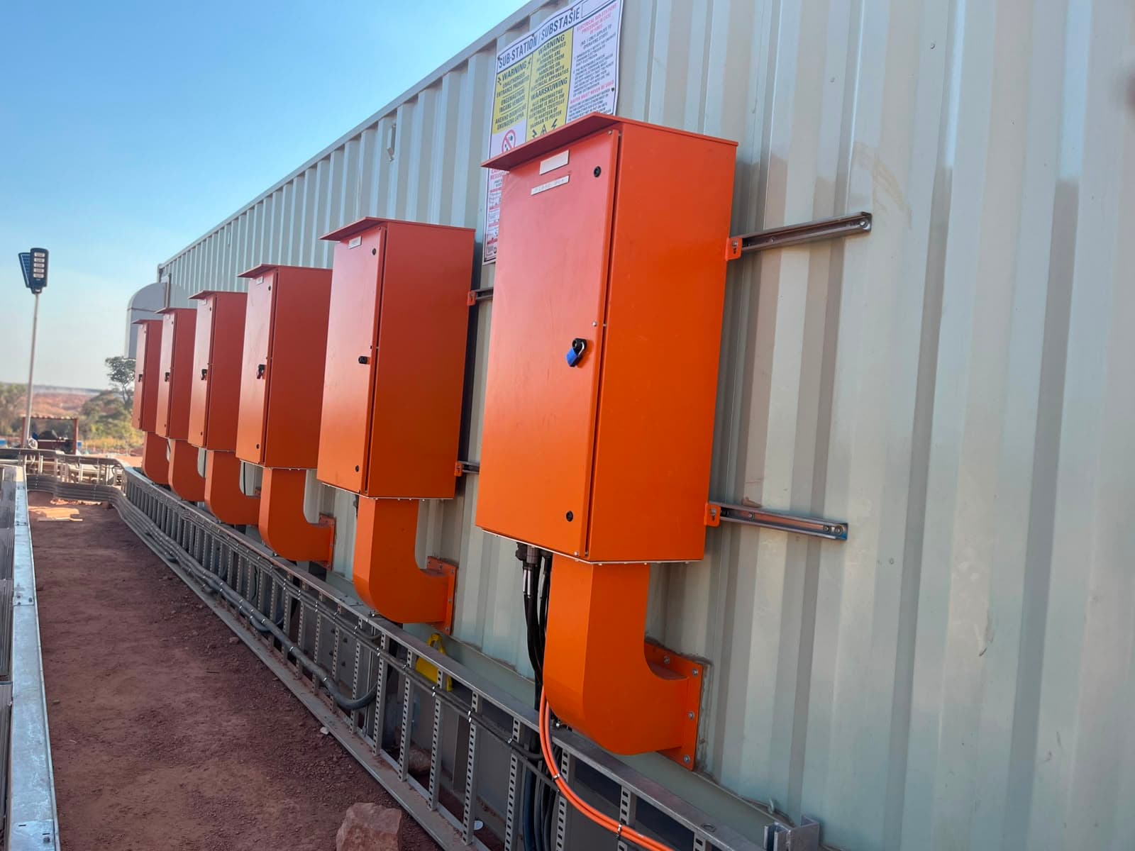 A row of orange Ivevane control enclosures mounted along a substation building on a mining site, with cable tray running beneath them.