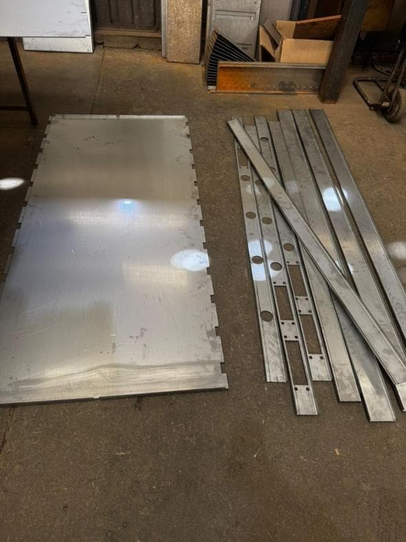 Cut steel plate and drilled flat bars laid out on the workshop floor
