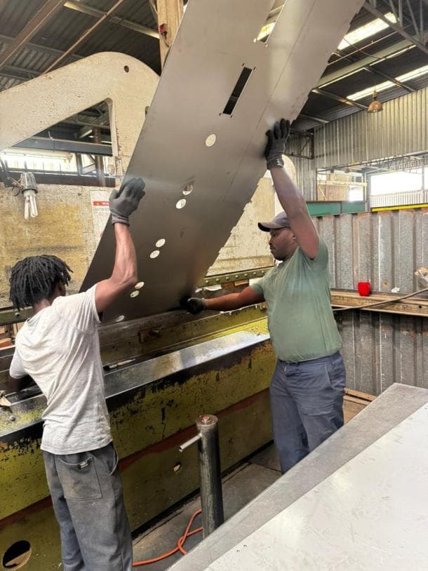 Two workers guiding a steel sheet on a press brake