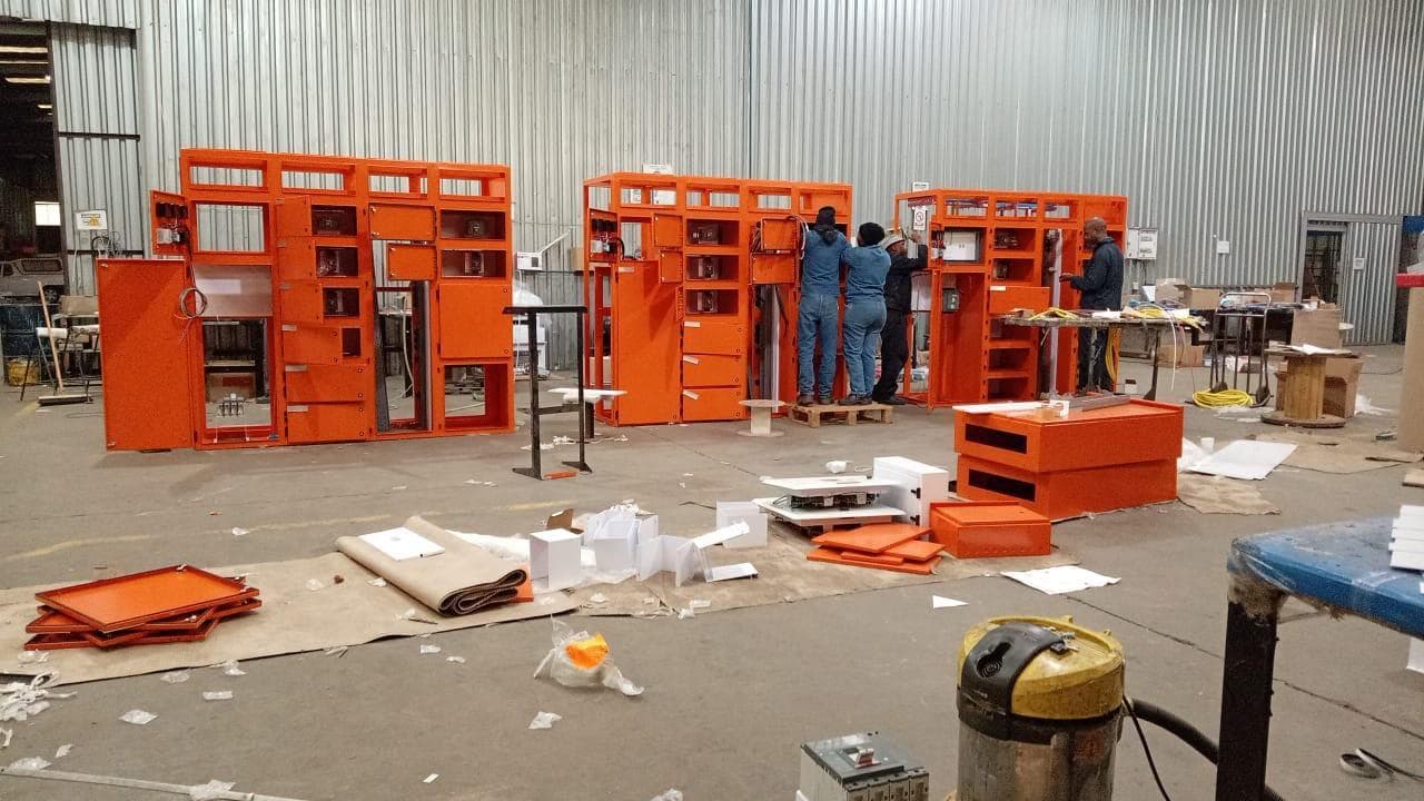Three orange feeder panels being wired and labelled by technicians in the workshop