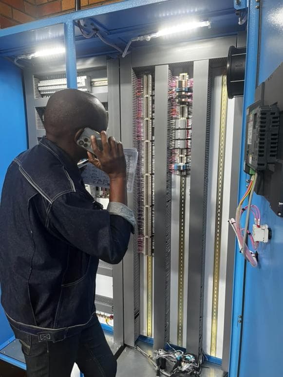 Technician at an open blue PLC panel with numbered wiring during commissioning